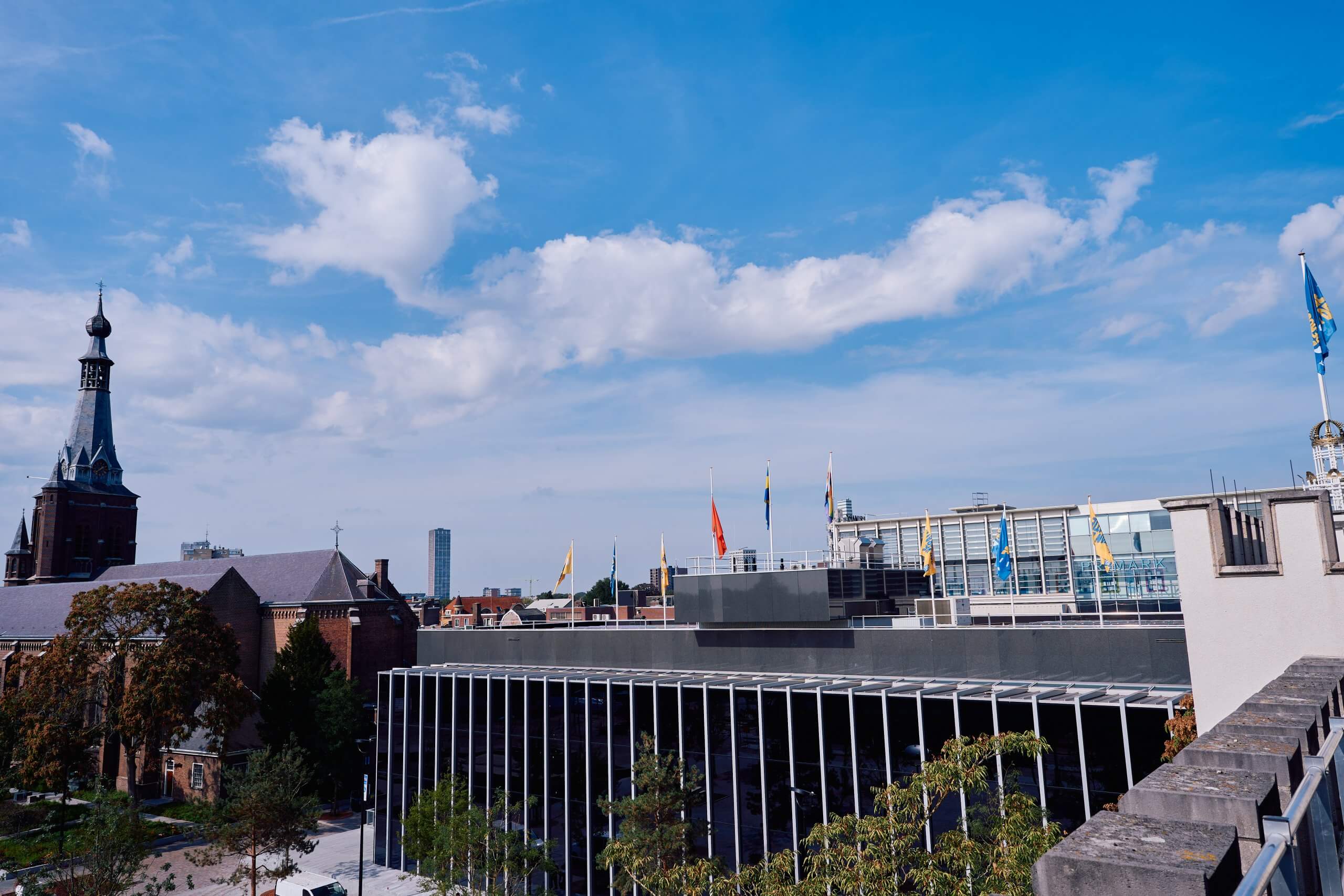 Een foto van de buitenkant van de raadszaal van bovenaf. Rechts de Heikese Kerk.